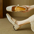 White Mary Jane flat shoes with twisted strap, pearl button detail, and low block heel