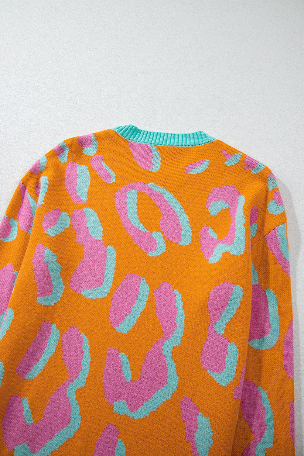 Women’s sweater close-up: orange, pink, and teal leopard-style pattern with ribbed crew collar.