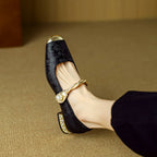 Black Mary Jane flat shoes with twisted strap, pearl button detail, and decorative heel trim