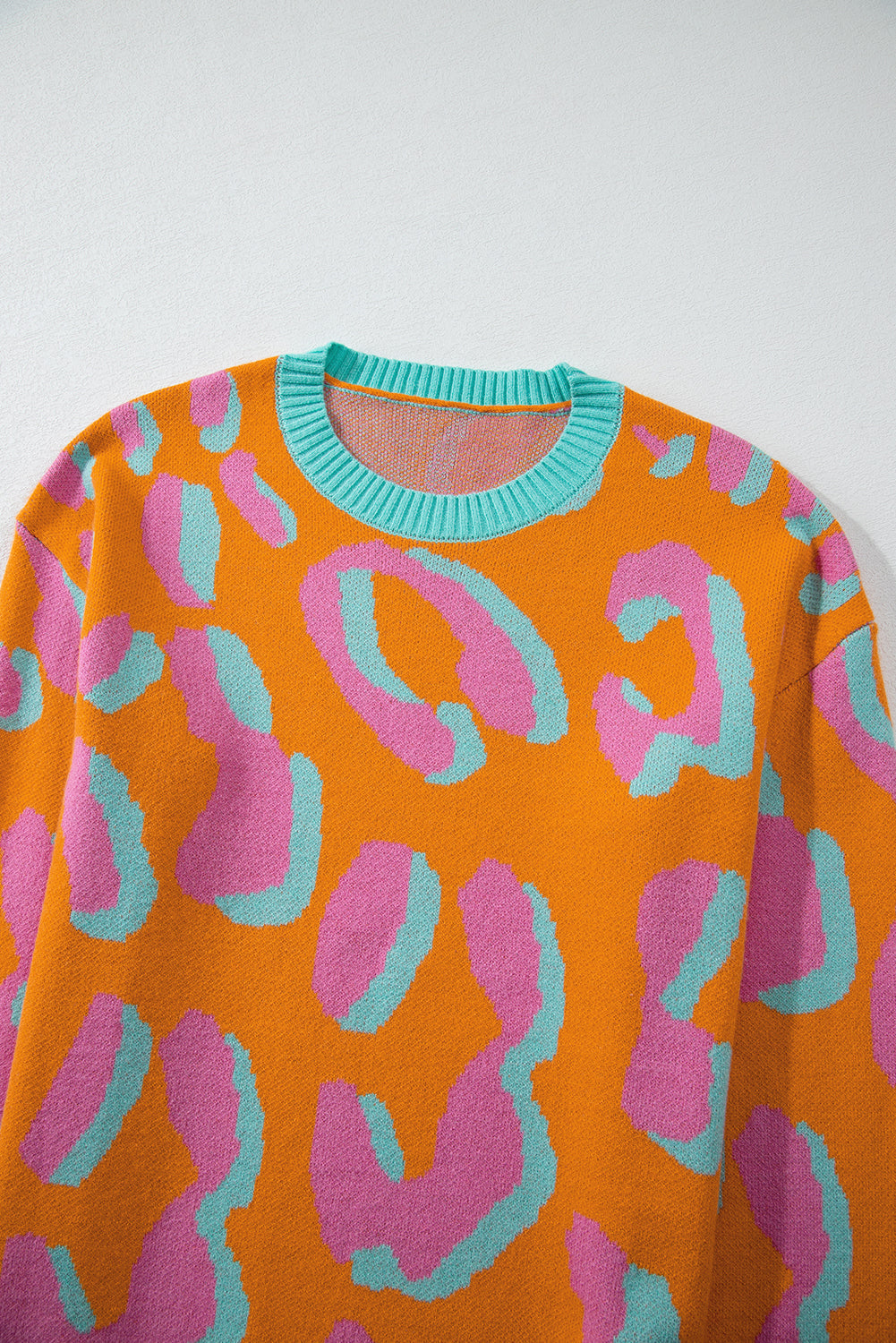 Women’s sweater close-up on neckline: orange, pink, and teal leopard-style print; ribbed crew neck.