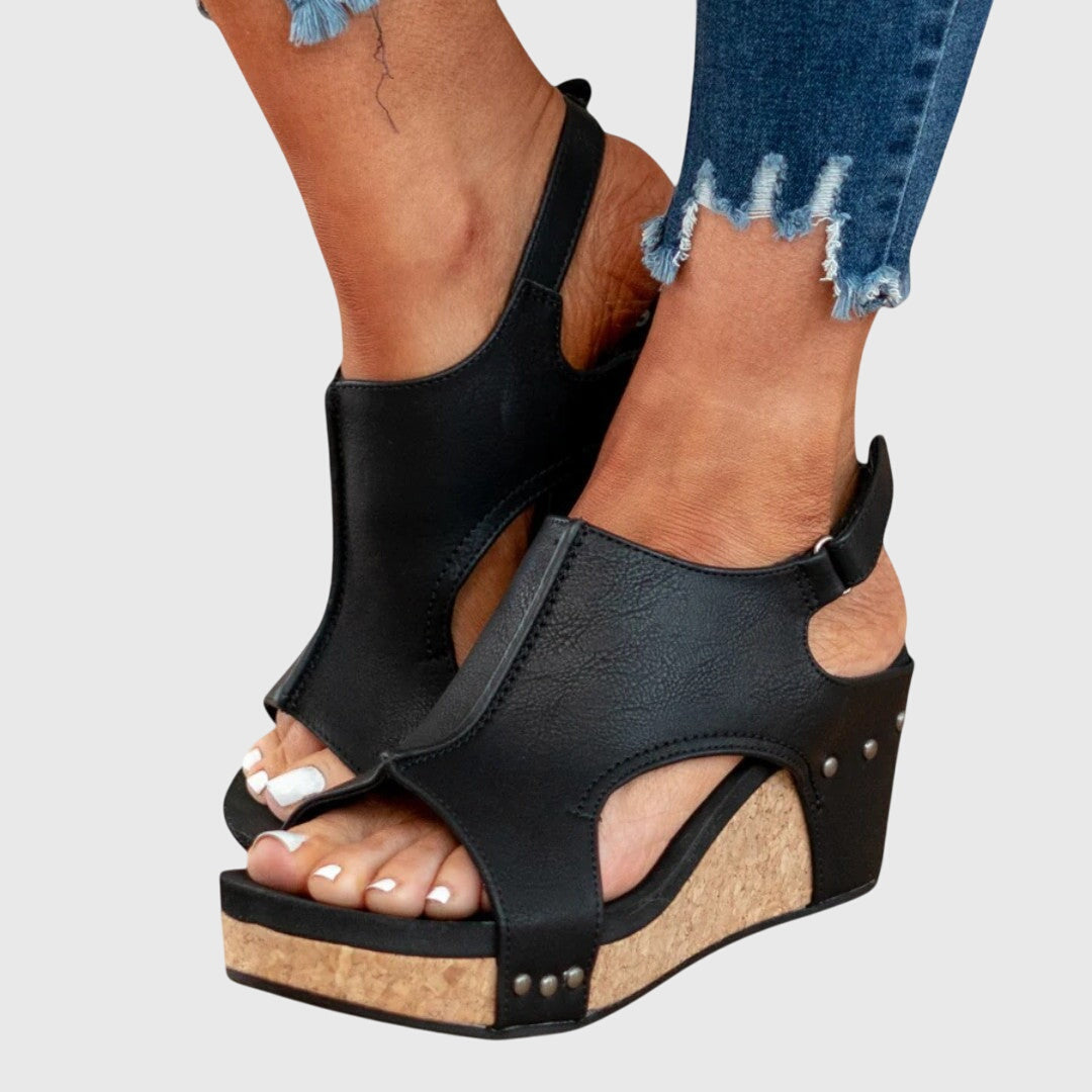 Black cushioned wedge sandals with open toe, ankle strap, and side stud accents.