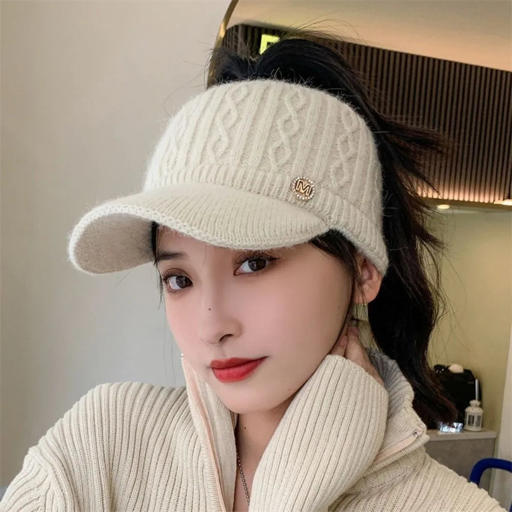 White knitted baseball cap with ribbed brim, cable-knit crown, and small M logo badge