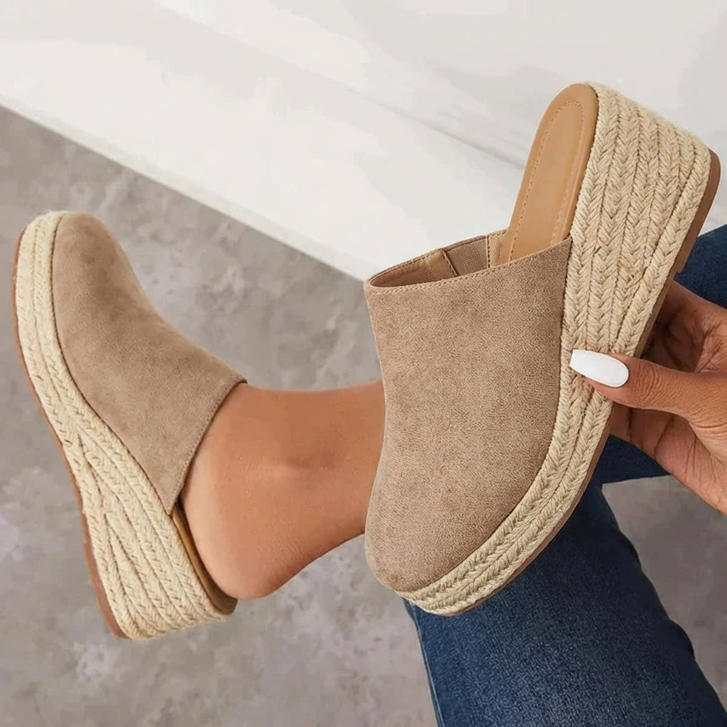 Beige suede-like closed-toe wedge mules with slip-on style and woven jute platform.