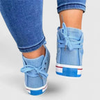 Light blue denim high-top sneakers from the heel view with lace bows and striped trim