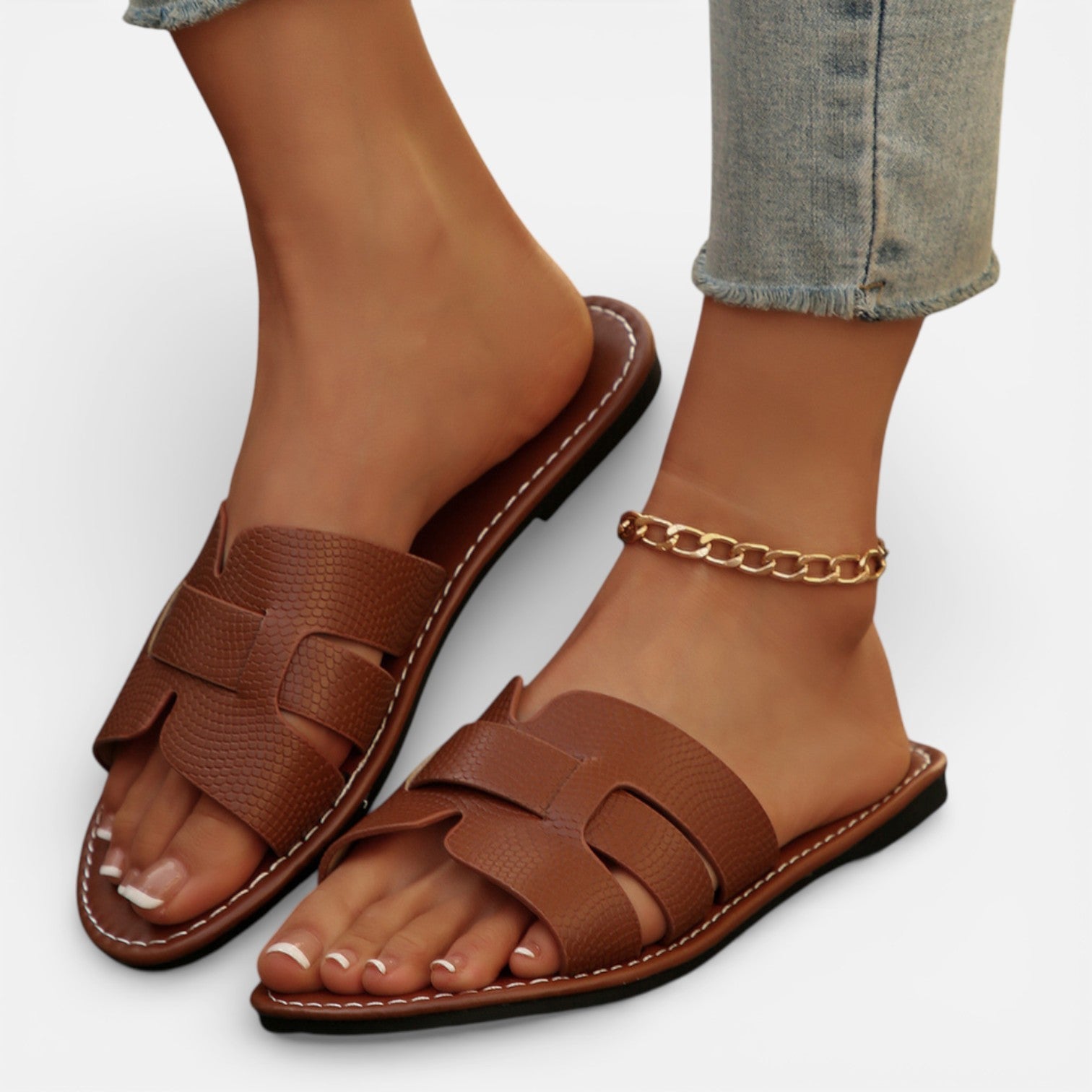 Women’s leather slide sandals, open toe, brown wide straps and ankle chain, flat cushioned sole.