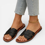 Women’s leather slide sandals, open toe, black wide straps and ankle chain, flat cushioned sole.