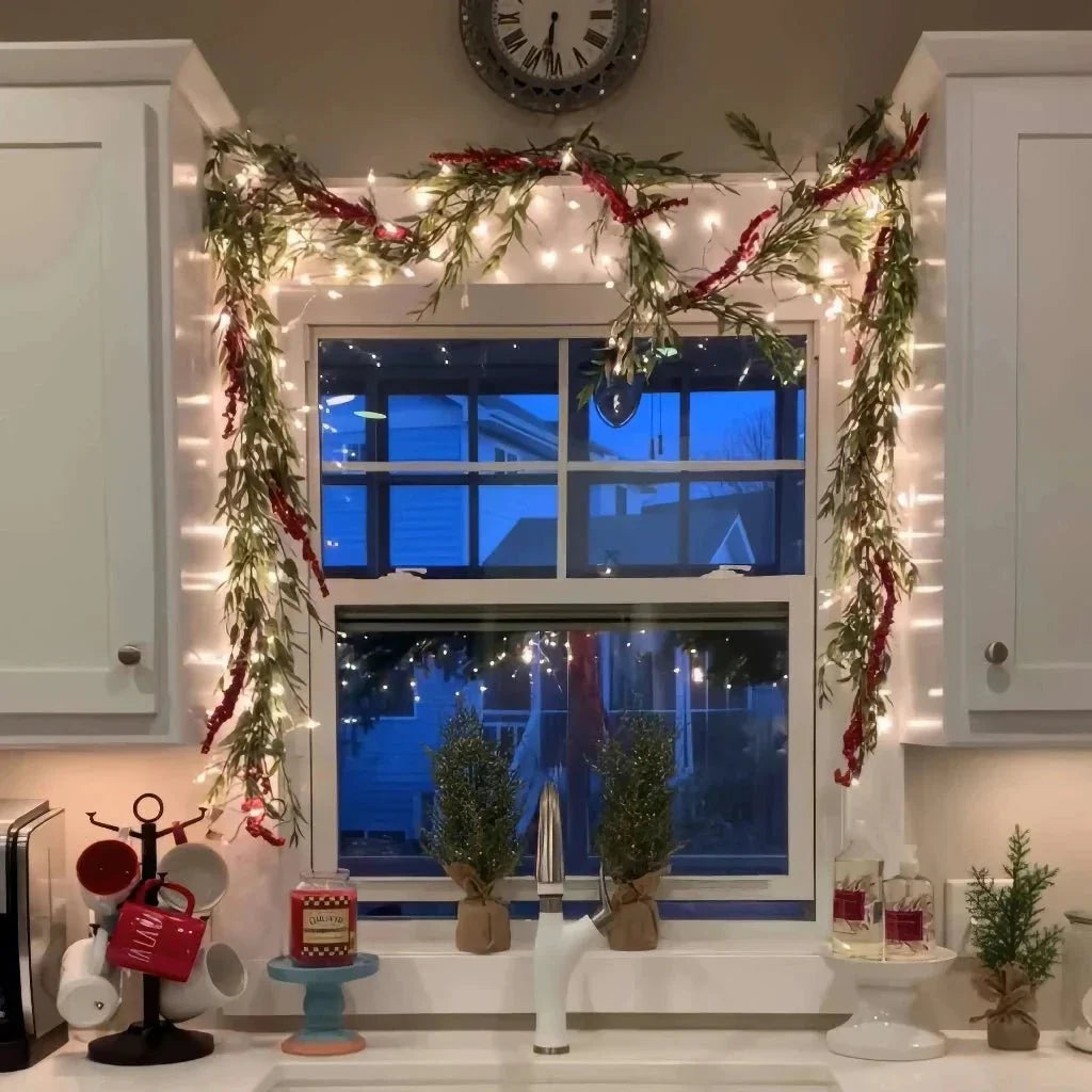 lighted holiday garland draped over window with warm fairy lights and evergreen bows