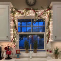 lighted holiday garland draped over window with warm fairy lights and evergreen bows