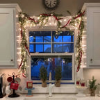 lighted holiday garland draped over window with warm fairy lights and evergreen bows