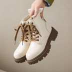 Women's white lace-up side-zip boots held by hand, rugged tread sole