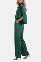 Green cape-sleeve jumpsuit side view with gathered waist and flowing wide legs.