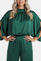 Green jumpsuit close-up: gathered high neckline and cinched waist at bodice.
