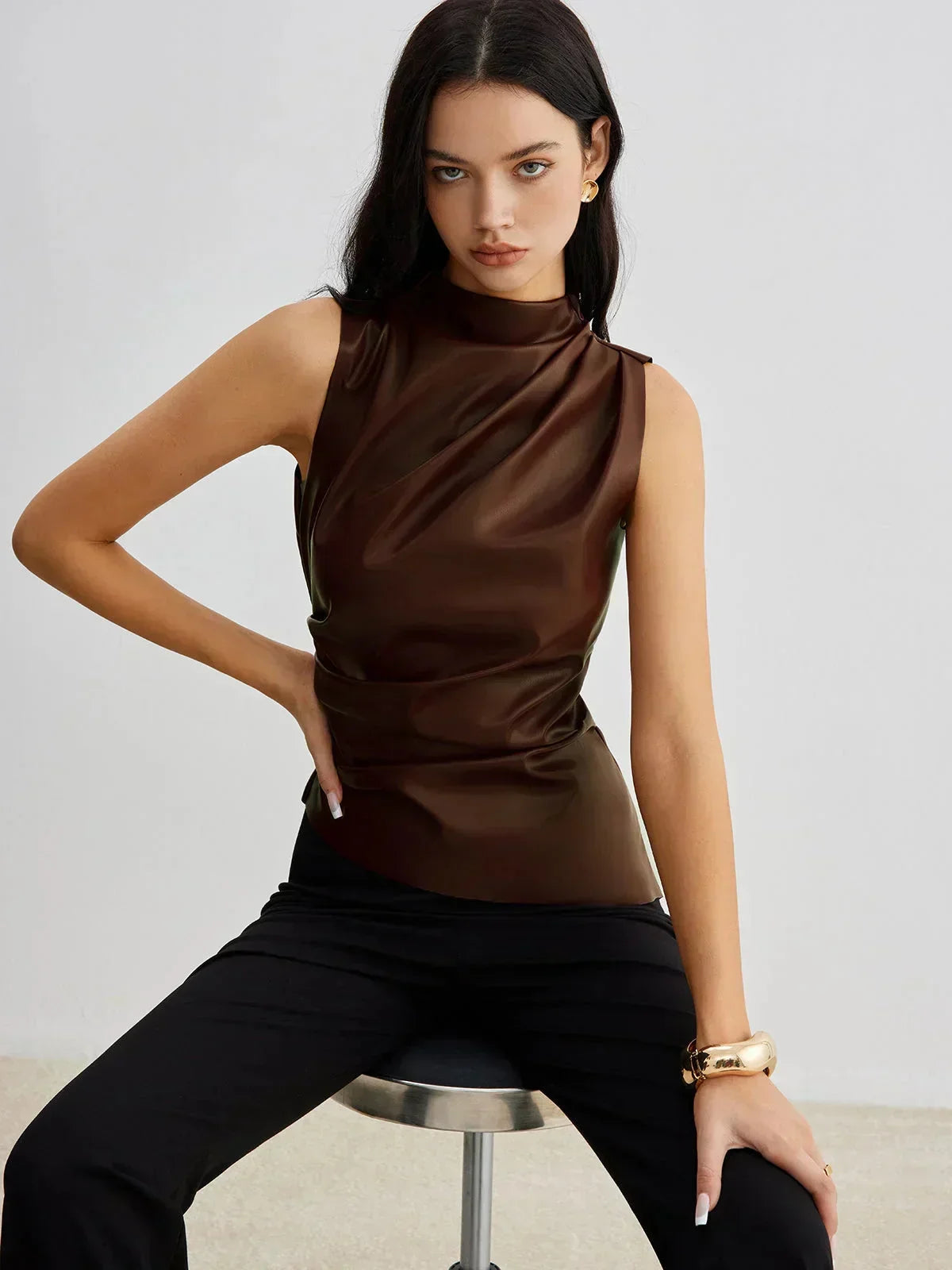 Dark brown sleeveless faux leather mock-neck top with draped front and fitted shape