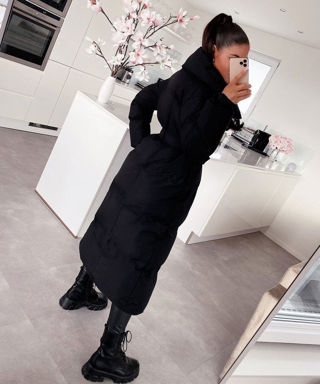 Women's long black puffer coat with hood, tie belt, and quilted back panels