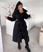 Women's long black puffer coat with hood, tie belt, and knee-length padded silhouette