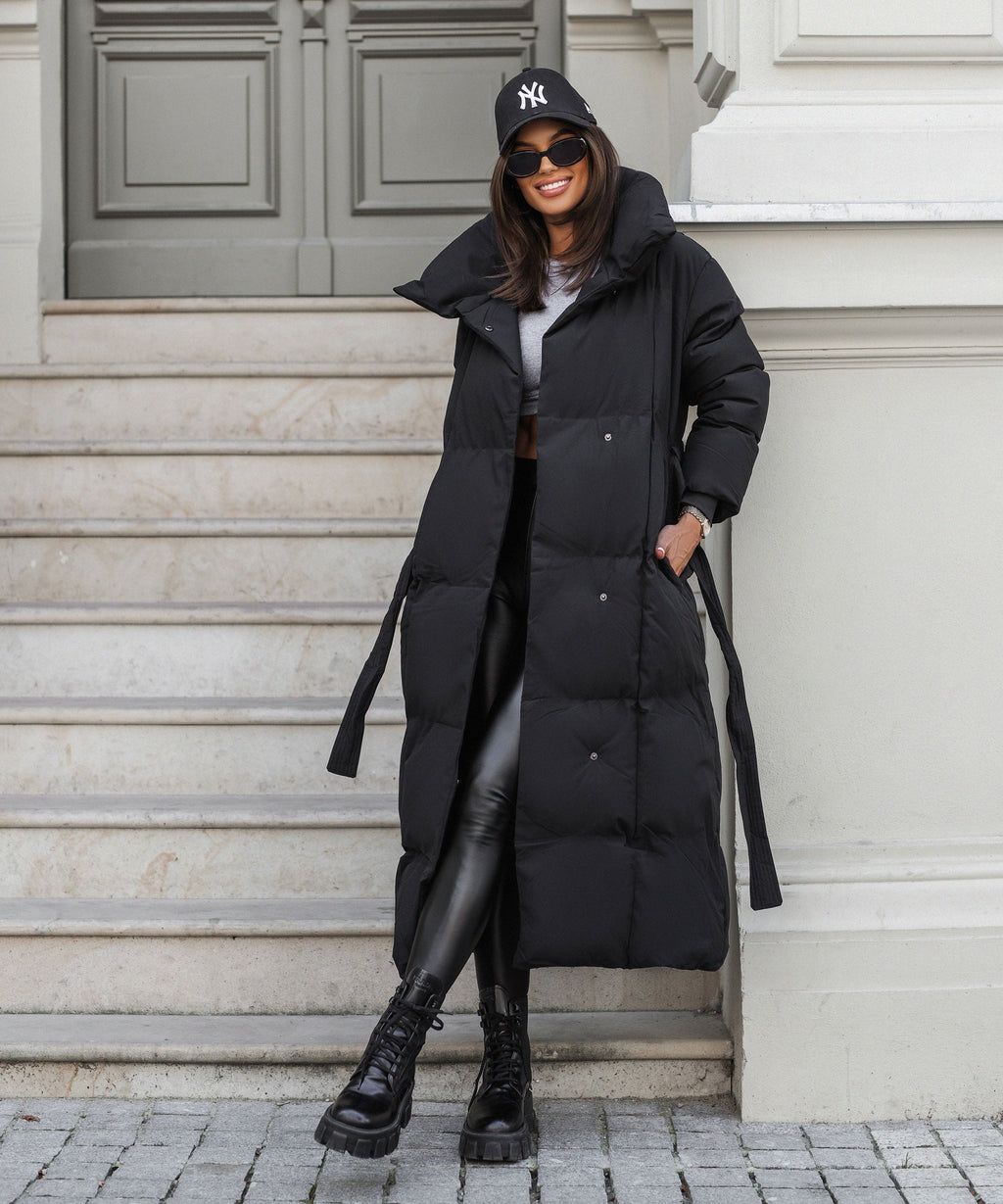 Black long puffer coat with hood up, tie belt at waist and quilted front