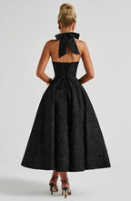 Black sleeveless A-line midi dress, open back with bow detail at top.