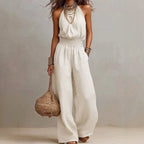 White sleeveless wide-leg jumpsuit with smocked waist and flowing wide trousers.