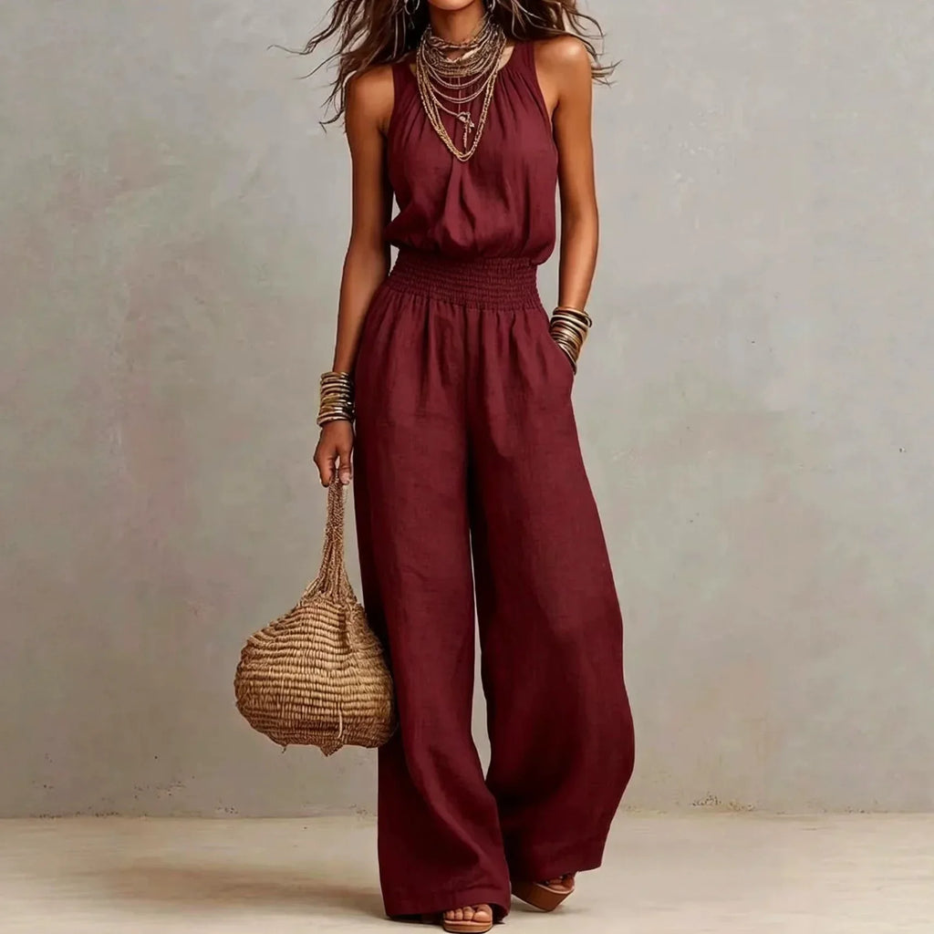 Burgundy sleeveless wide-leg jumpsuit with smocked waist and loose flowing pants.