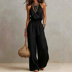 Black sleeveless wide-leg jumpsuit with smocked waist and flowing wide trousers.
