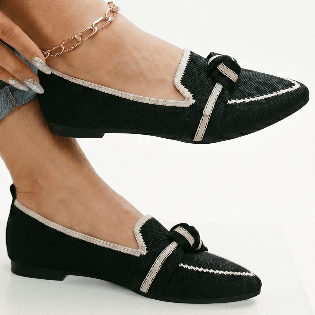 Black slip-on loafers with white trim and knotted bow