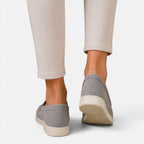 Women's gray slip-on loafers on feet with rounded heel and stitched back seam
