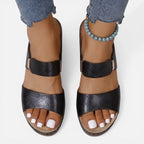 Black leather block heel sandals with open toe, wide straps, and bead ankle bracelet
