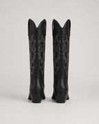 Black knee-high cowboy boots with ornate embroidered swirl motifs and stacked heel