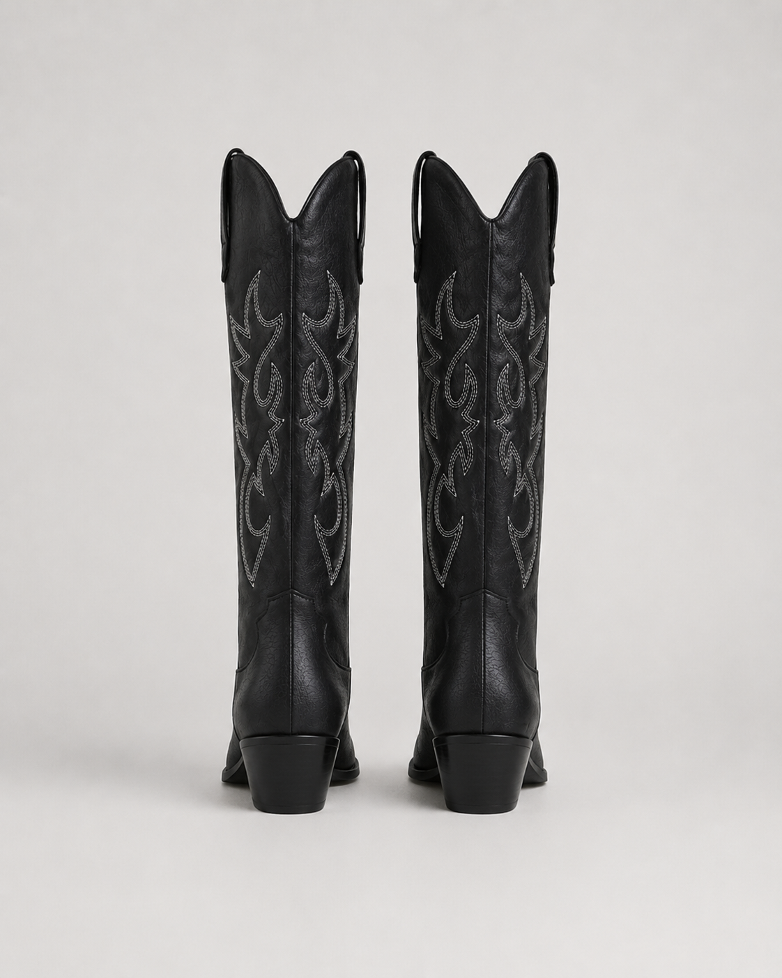 Black knee-high cowboy boots with ornate embroidered swirl motifs and stacked heel