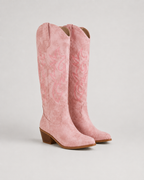 Pink knee-high cowboy boots with embroidered swirl motifs and low block heel