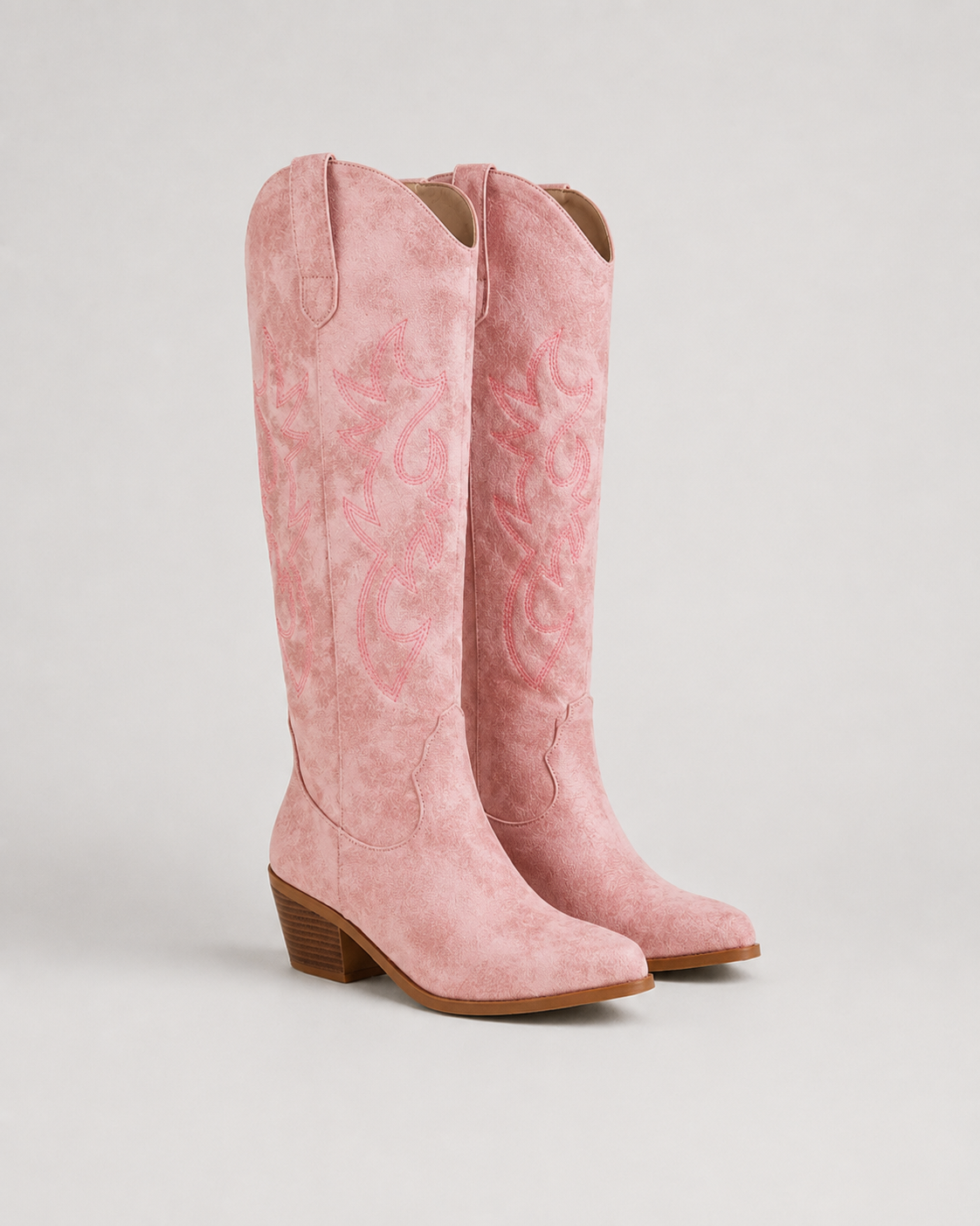 Pink knee-high cowboy boots with embroidered swirl motifs and low block heel