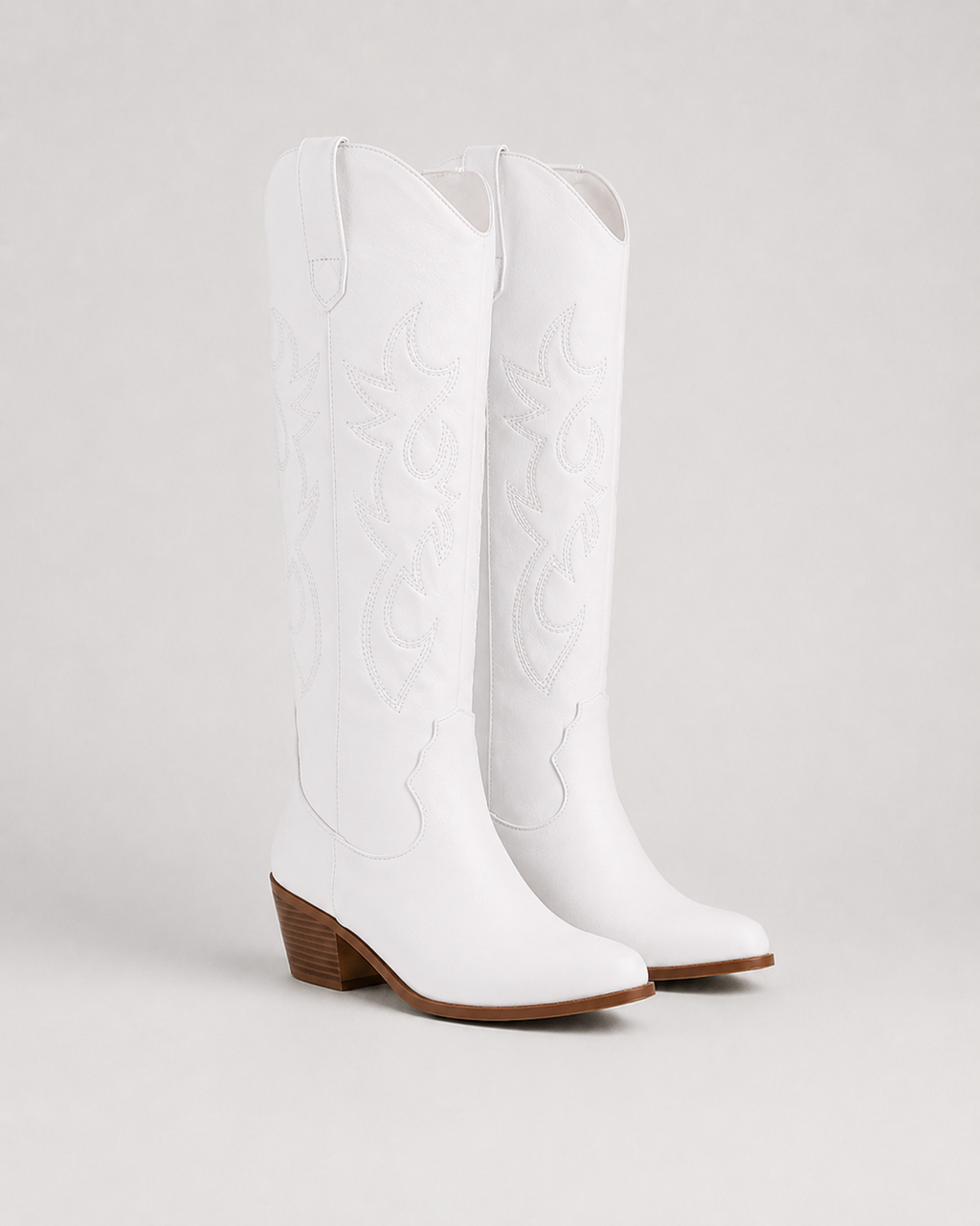 White knee-high cowboy boots with embroidered swirl pattern and low block heel