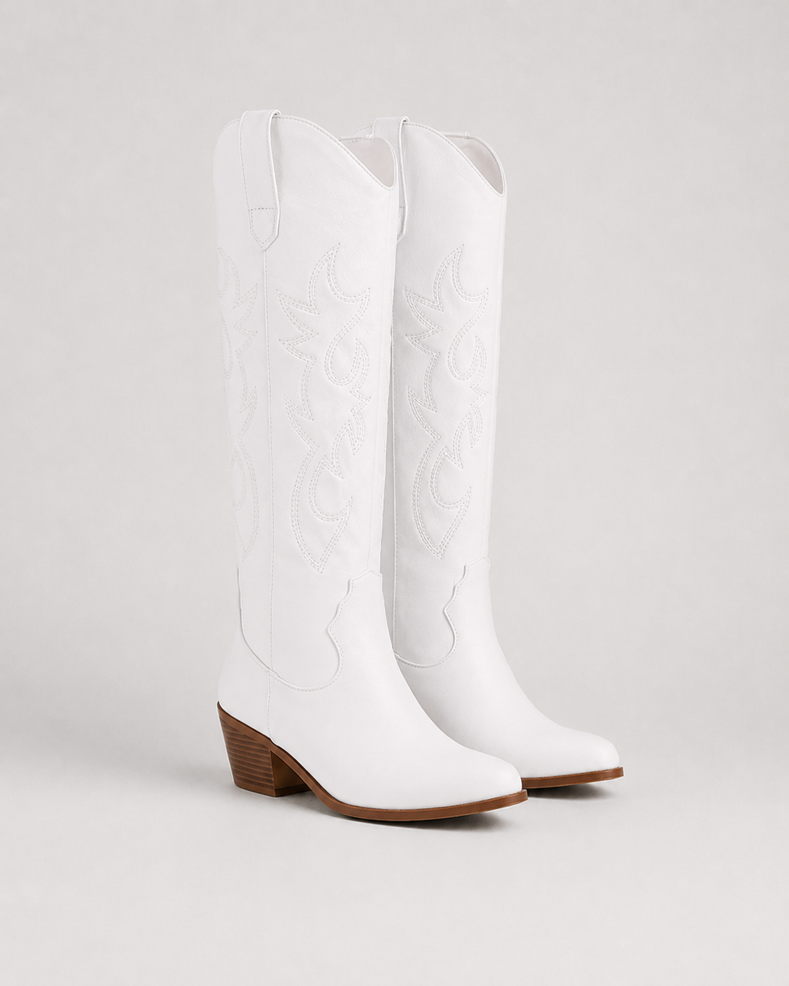 White knee-high cowboy boots with embroidered swirl pattern and low block heel