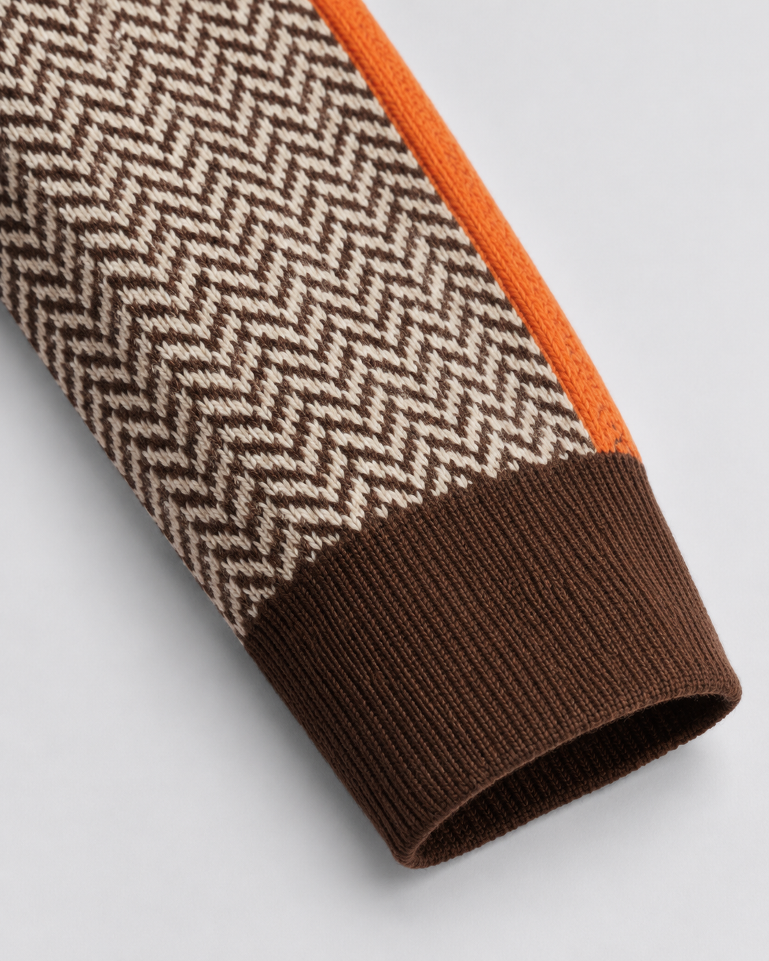 Ribbed knit cuff on herringbone sweater sleeve with dark brown and orange trim