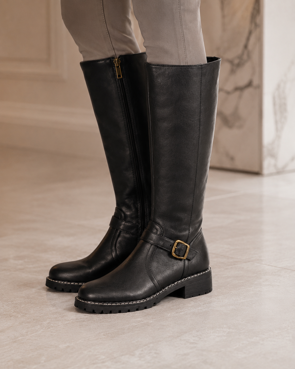 Black knee-high buckle boots with side zip and lug sole, worn on tiled floor.