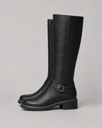 Black knee-high buckle boot with side zip, buckle strap and lug sole.