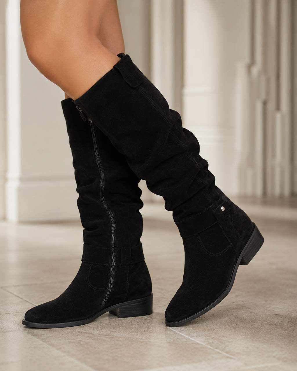 Black suede knee-high boots with low heel, side zip, and top cuff strap