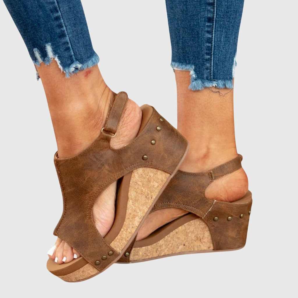 Brown cushioned wedge sandals with crisscross straps and stud accents on the upper.