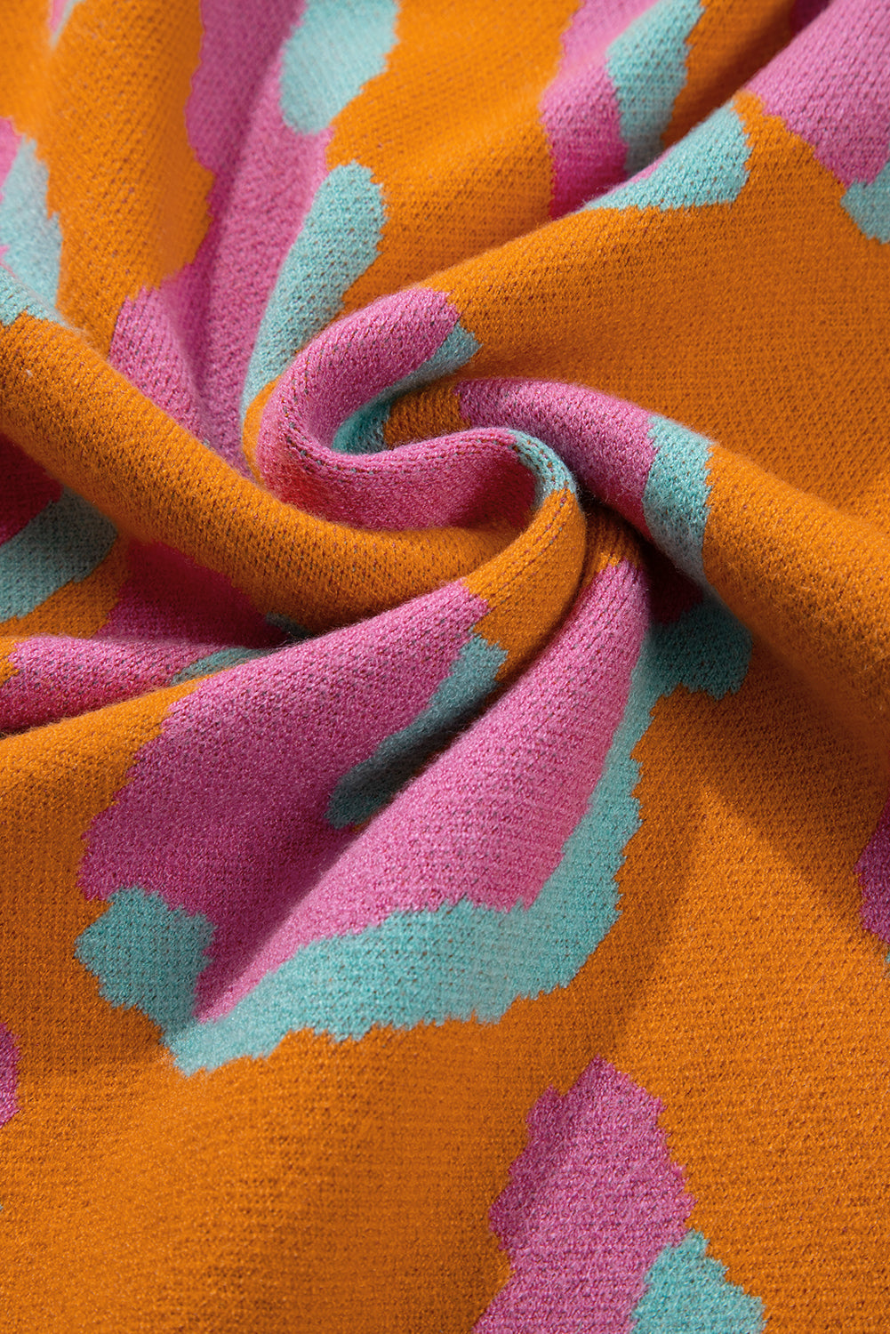 Close-up knit fabric in orange with pink and teal leopard-style colorblock pattern.