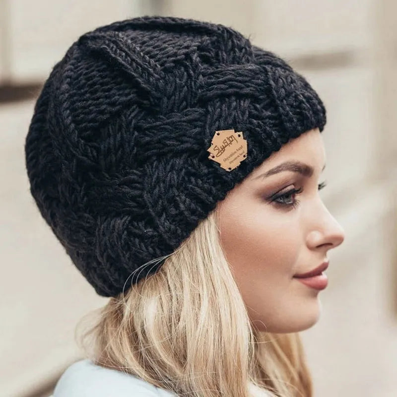 Black knitted beanie hat with textured cable pattern and brown brand patch