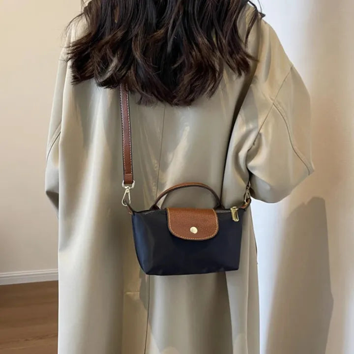 Mini crossbody bag in dark blue with tan flap and gold-tone clasp, worn on the shoulder