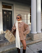 Light brown loose-fit women’s coat with large lapels and button front, holding bag.