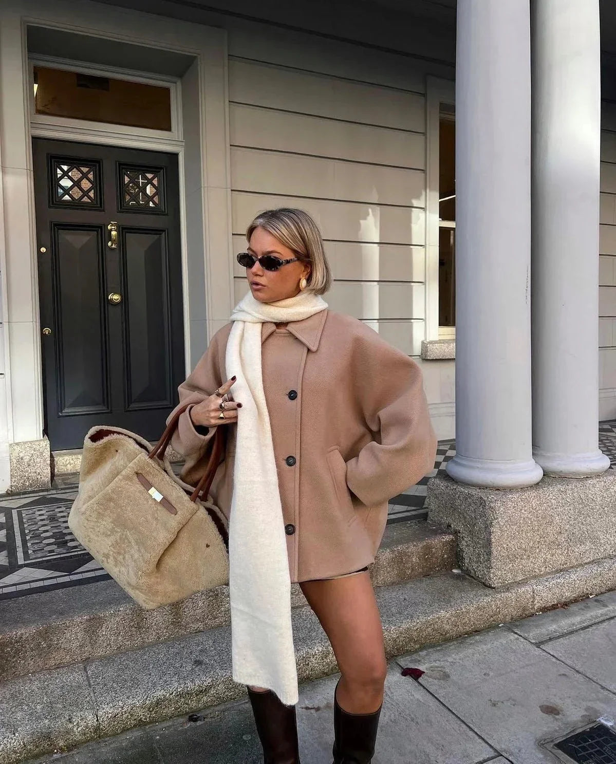 Light brown loose-fit women’s coat with large lapels and button front, holding bag.