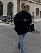 Black loose-fit women’s coat with oversized lapels and button closure, walking view.