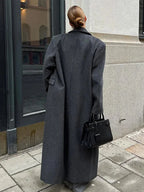 Women’s long coat, dark gray, back view with wide lapels and buttoned sleeve cuffs