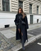 Women's long black belted coat with wide lapels and button front, side view