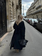 Back view of women's long black belted coat with wide lapels