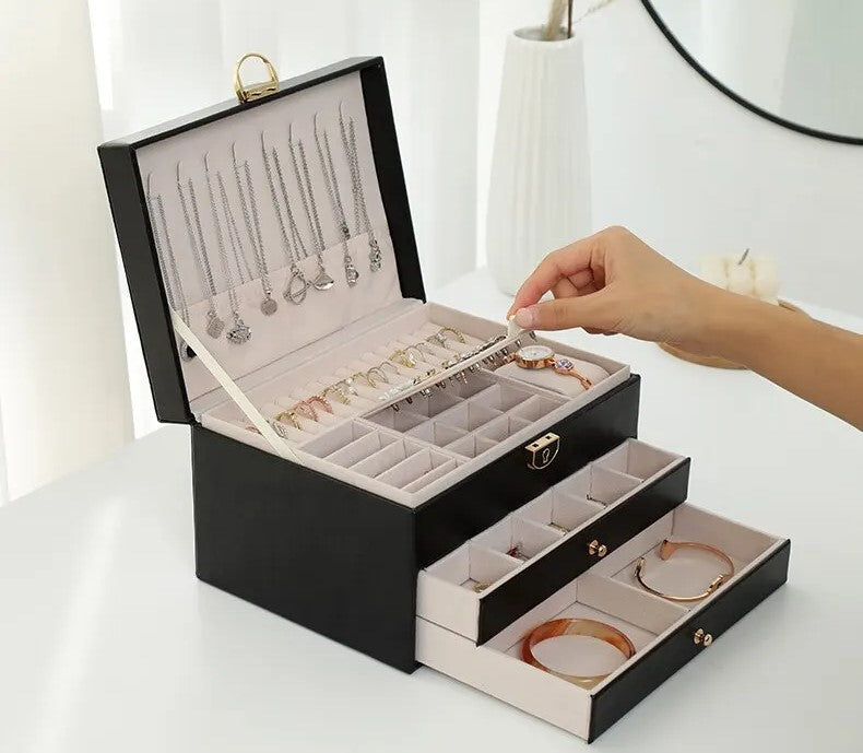 Black leather jewelry box open with layered trays and a hand arranging necklaces