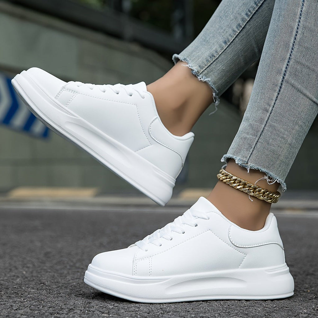 White lace-up trainers with thick sole, black side and heel accents, on pavement with jeans
