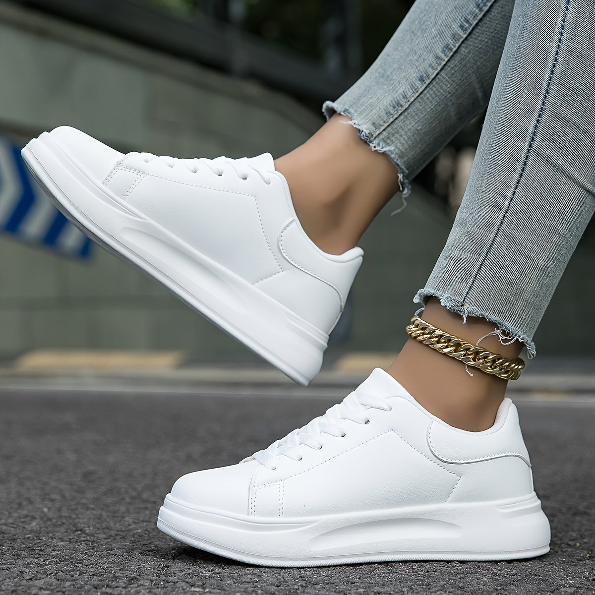 White lace-up trainers with thick sole, black side and heel accents, on pavement with jeans